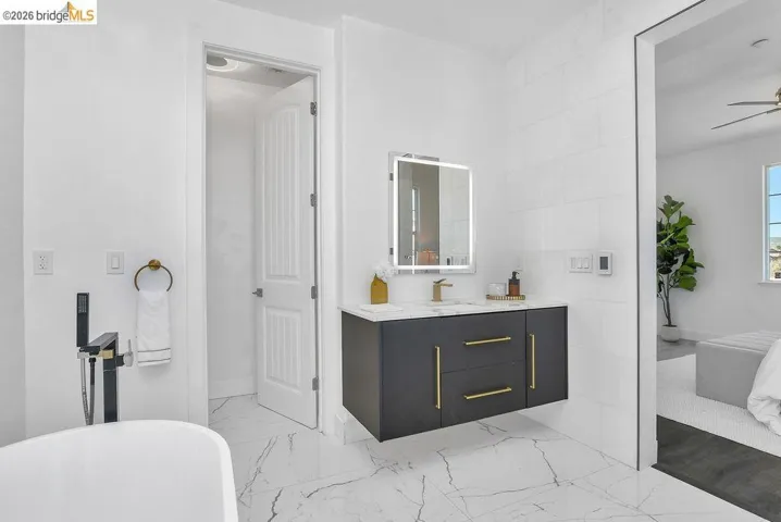 Ensuite bathroom with vanity, light marble finish floors, a soaking tub, a ceiling fan, and tile walls