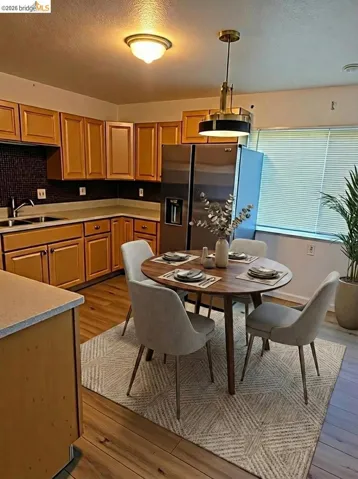 Kitchen with stainless steel fridge with ice dispenser, a textured ceiling, light countertops, light wood-style floors, and pendant lighting