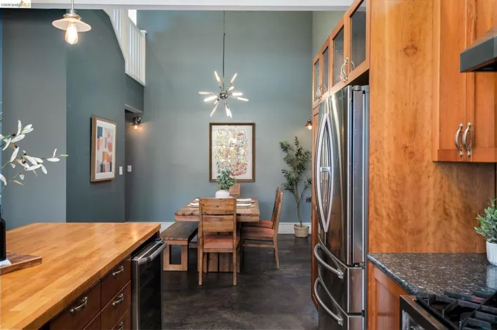 Kitchen featuring glass insert cabinets, finished concrete floors, freestanding refrigerator, a high ceiling, and range hood