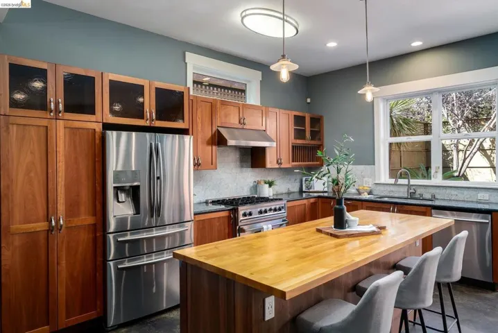 Kitchen with wood counters, stainless steel appliances, glass insert cabinets, hanging light fixtures, and a kitchen breakfast bar