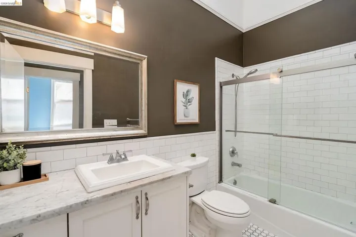 Bathroom with vanity, tile walls, shower / bath combination with glass door, and a wainscoted wall