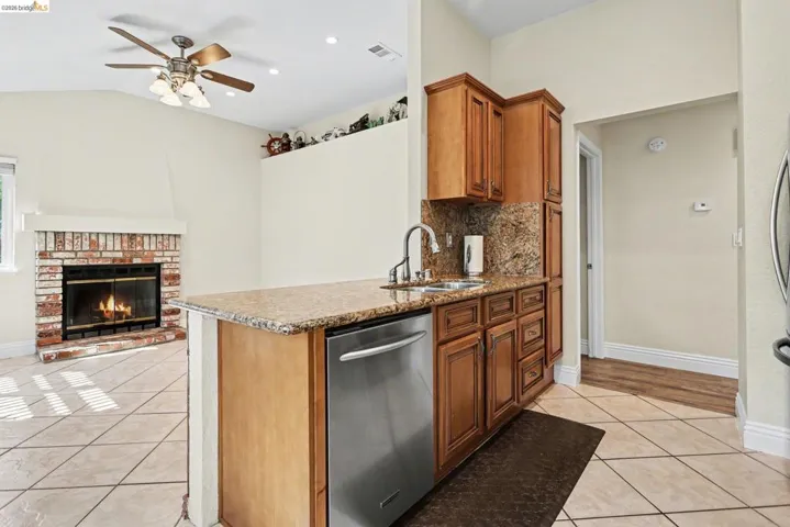 Kitchen featuring light stone counters, stainless steel dishwasher, open floor plan, wood finish cabinetry, and lofted ceiling