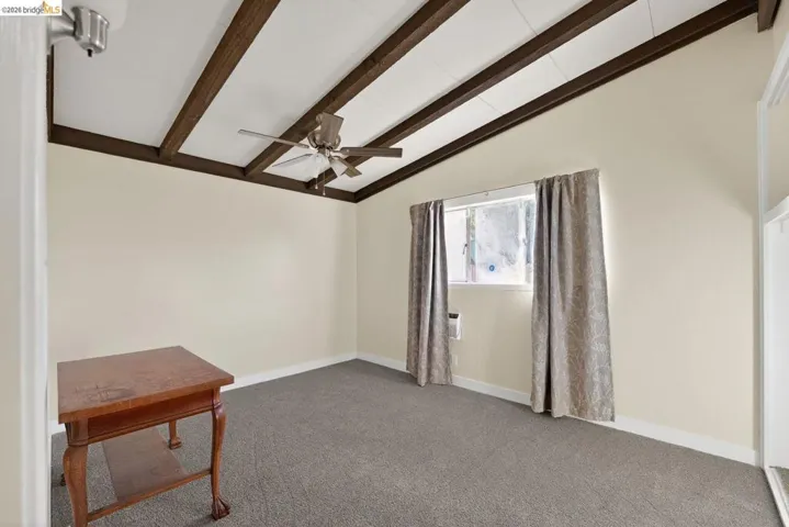 spare room with carpet, ceiling fan, and vaulted ceiling with beams