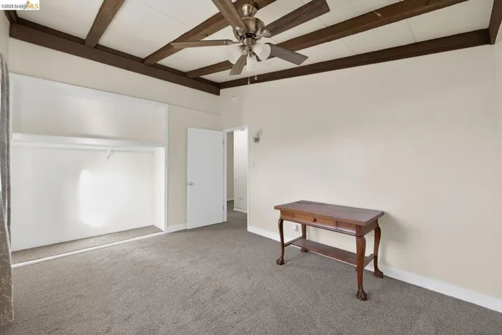 unfurnished bedroom featuring carpet flooring, a ceiling fan, and beamed ceiling