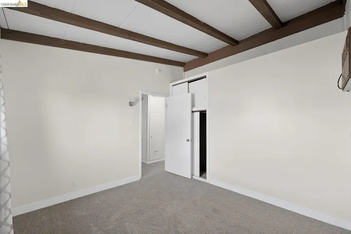 unfurnished bedroom with carpet, a closet, and beam ceiling