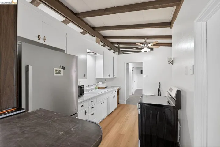 kitchen featuring white cabinets, light countertops, freestanding refrigerator, washer / dryer, and beam ceiling