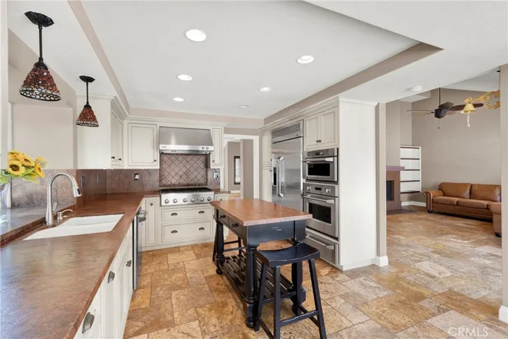 Another view of remodeled kitchen, shows upgraded custom stainless cooktop and hood, built-in frdge, microwave and oven. Custom cabinets with upgraded hardware, pendant lighting over sinks and recessed lighting. Opens to the attached family room.