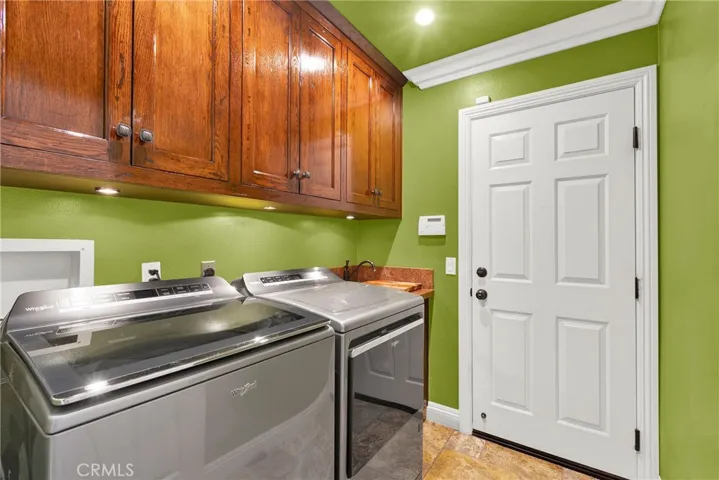 Indoor Laundry Room off garage. Custom Panel Door and Hardware. Crown Molding. Wet Sink and Cabinets with Under Lighting. Recessed Lights. Travertine Flooring.