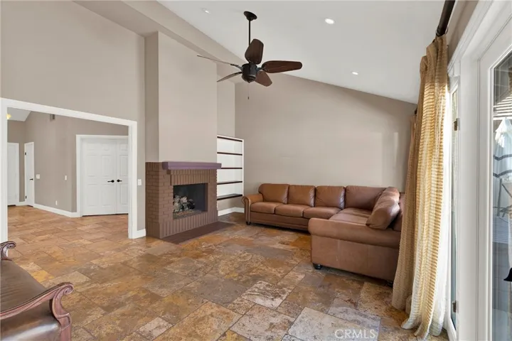 Family Room is open to the kitchen, the living room and the exterior patio and backyard. Vaulted ceilings, recessed lights, ceiling fan, travertine flooring, and center room fireplace.