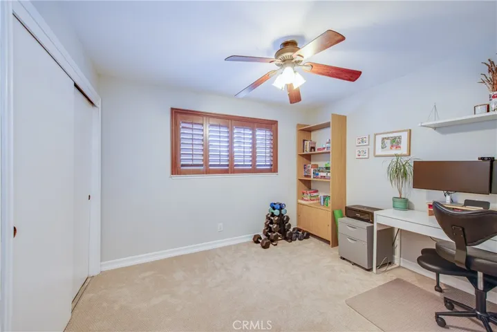 Bedroom 2 has a ceiling fan and large window with plantation shutters and overlooks the backyard.