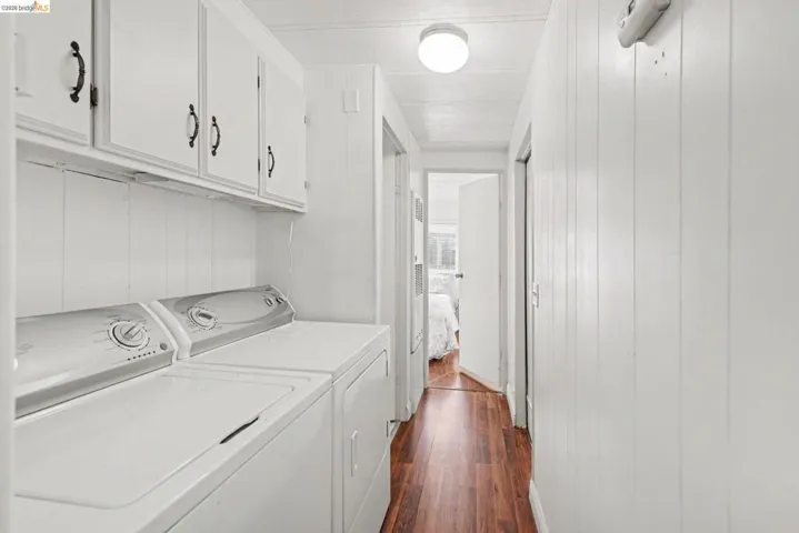 Laundry area with dark wood-type flooring, washer and dryer, cabinet space, and wooden walls