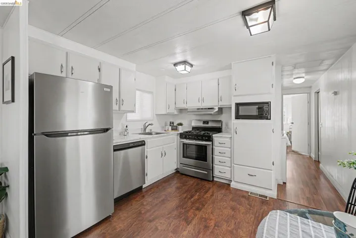 Kitchen with stainless steel appliances, white cabinets, light countertops, and dark wood-style flooring
