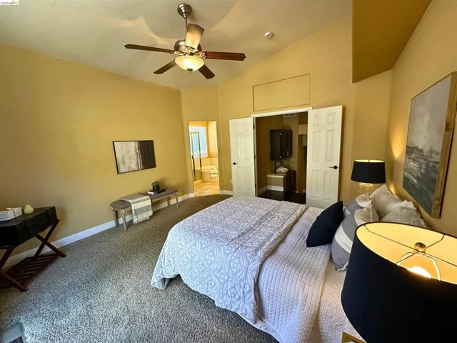 Carpeted bedroom with ensuite bathroom, lofted ceiling, and ceiling fan