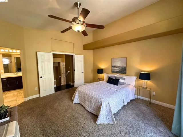 Carpeted bedroom featuring ceiling fan, ensuite bath, and a high ceiling