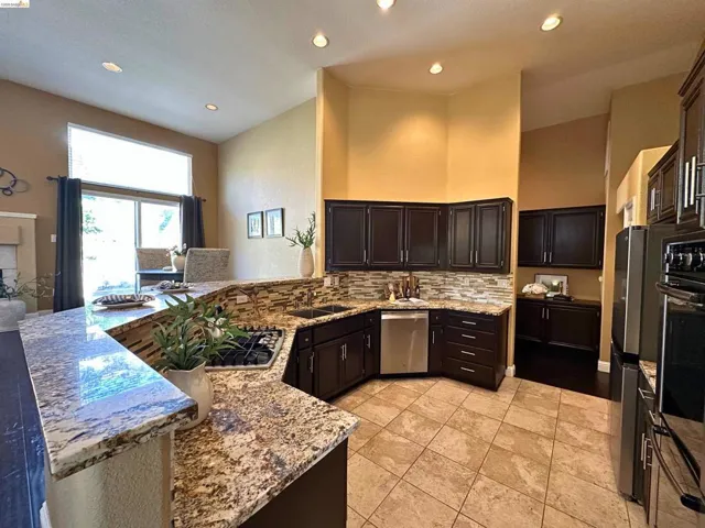 Kitchen featuring a peninsula, decorative backsplash, recessed lighting, stainless steel appliances, and light stone counters