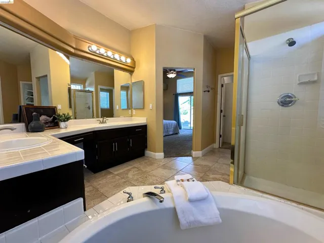 Full bath featuring a shower stall, connected bathroom, vanity, a ceiling fan, and a garden tub