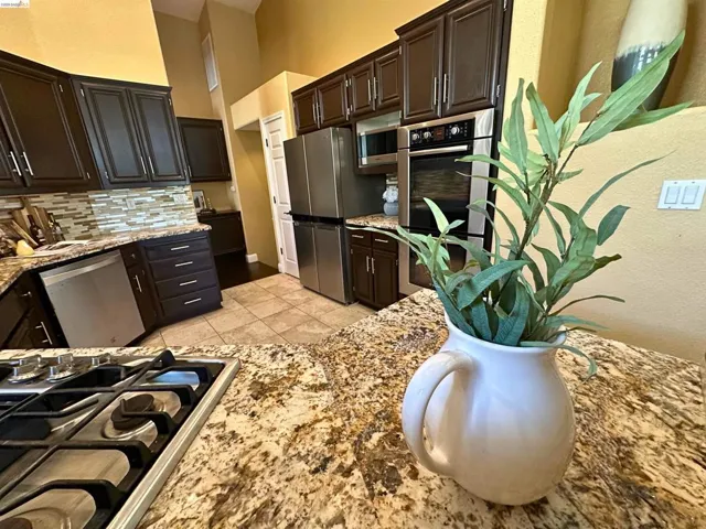 Kitchen featuring stainless steel appliances, light stone countertops, decorative backsplash, a high ceiling, and dark wood finish cabinetry