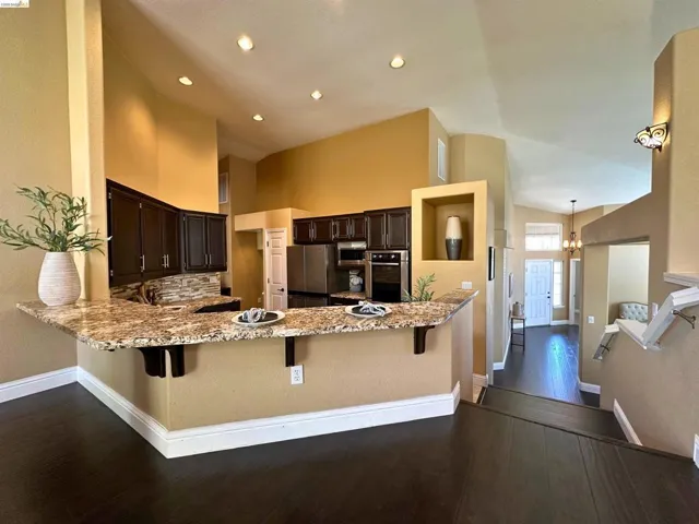 Kitchen featuring a kitchen bar, a peninsula, dark wood finish cabinetry, hanging lights, and light stone countertops
