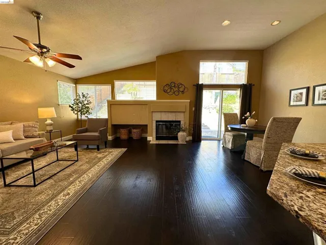 Living area with a ceiling fan, a textured wall, dark wood-type flooring, and a fireplace