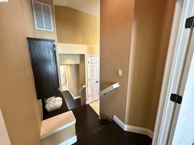 Hallway featuring an upstairs landing, a textured wall, and lofted ceiling