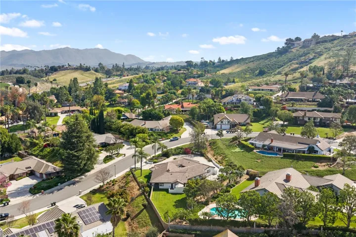Sweeping aerial view captures the surrounding neighborhood, rolling hills, and scenic setting. The location offers a peaceful residential atmosphere with a picturesque backdrop.