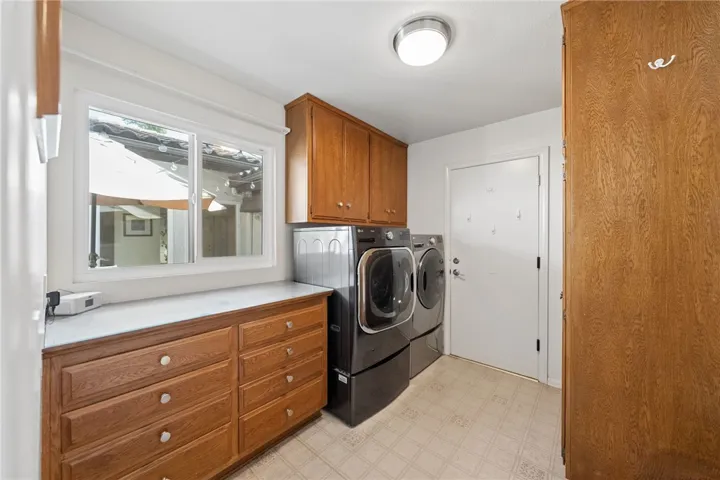 Dedicated laundry room with side-by-side washer and dryer, extensive cabinetry, and additional counter space for folding and storage. A window brings in natural light for a bright, practical workspace.