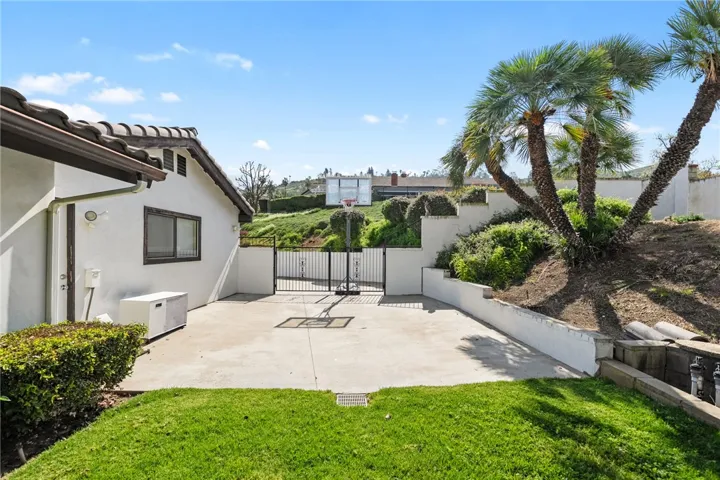 Private backyard includes a paved sport court area with basketball hoop, framed by mature palms and terraced landscaping. A versatile outdoor feature for recreation and everyday enjoyment.