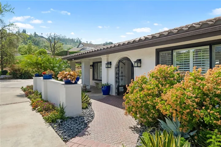 Brick-accented walkway and courtyard-style entry create a warm, inviting approach, complemented by colorful planters and established garden beds.