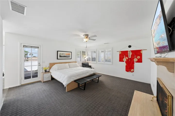 Oversized primary bedroom with room for a sitting area, plantation shutters, and direct outdoor access through French doors. A fireplace adds warmth and a comfortable retreat-like feel.