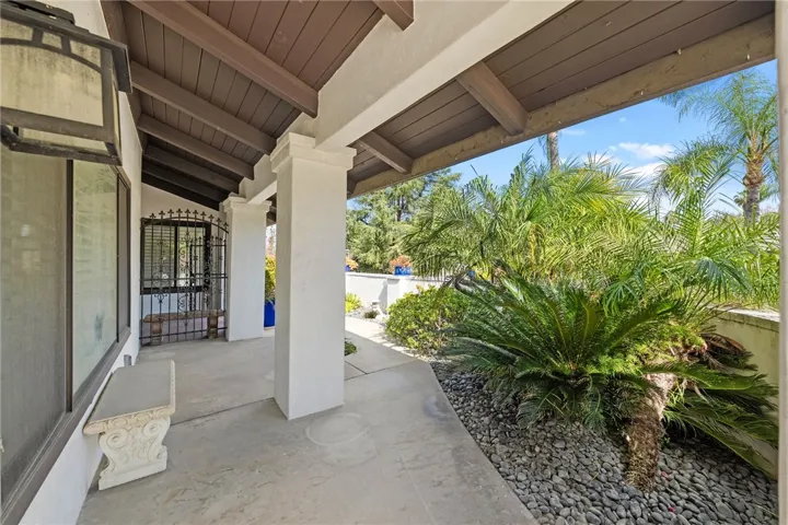 Covered front porch with substantial columns, exposed beams, and a gated entry detail that adds character to the arrival experience. Lush tropical landscaping softens the approach.
