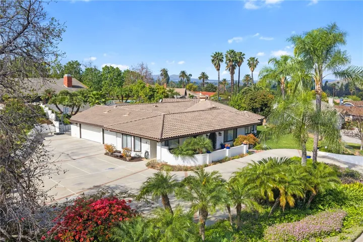 Elevated exterior view highlights the home’s broad footprint, manicured grounds, and attractive corner-lot presence. Mature trees and palms frame the property beautifully.
