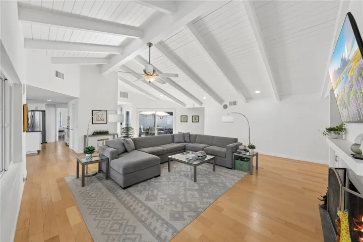 Spacious living room with vaulted beamed ceilings, wide-plank flooring, and an open layout anchored by a fireplace. Large sliding doors provide easy access to the patio and bring in natural light.