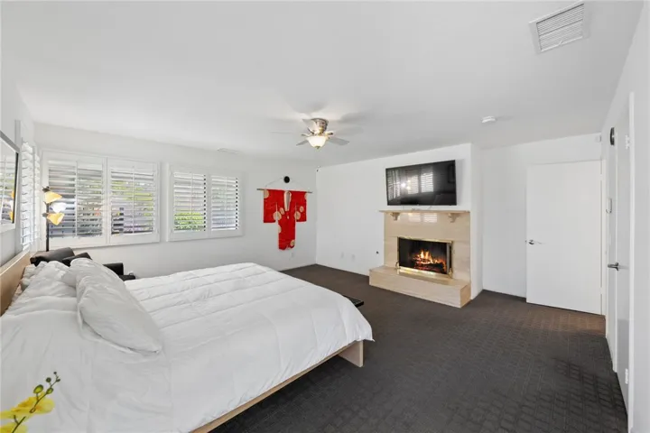 Spacious primary suite featuring a fireplace, wall-mounted media space, and abundant room for a full bedroom setup. Plantation shutters and clean finishes complete the polished look.