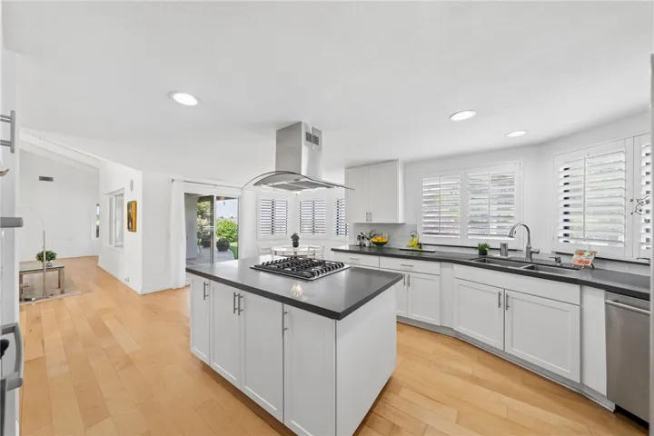 Bright, updated kitchen with crisp white cabinetry, quartz countertops, stainless steel appliances, and a large center island with cooktop. Multiple windows and a nearby glass door enhance the airy feel and everyday functionality.