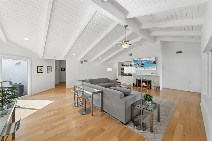 Open-concept living room with dramatic vaulted ceilings, exposed beams, and a fireplace flanked by built-in shelving and cabinetry. Wide-plank flooring and expansive wall space add to the room’s flexibility and scale.