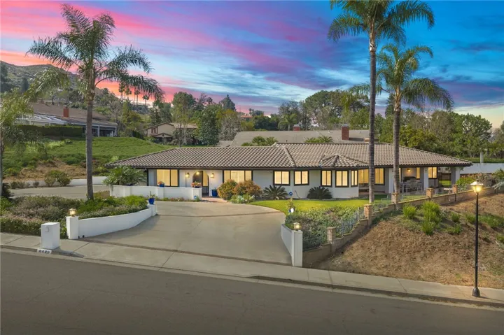 A welcoming single-story exterior with a wide circular driveway, mature palms, and polished curb appeal. The spacious frontage creates an impressive first impression.
