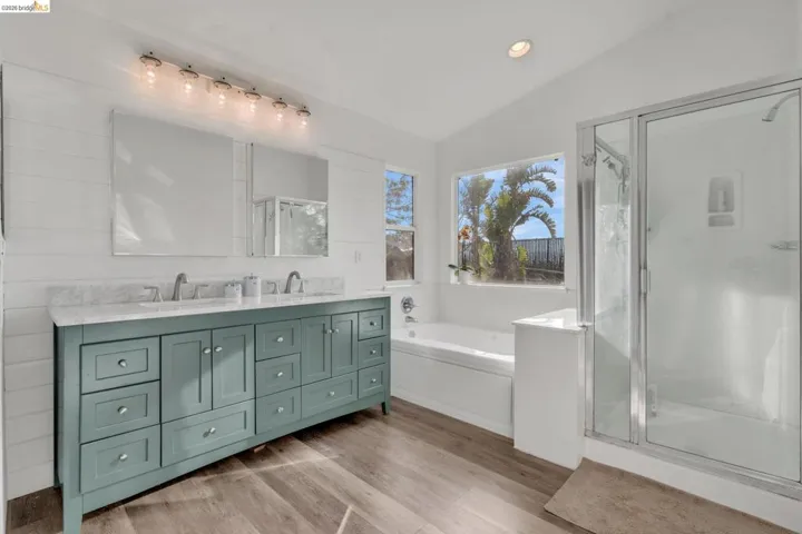 Bathroom featuring vaulted ceiling, double vanity, recessed lighting, a bath, and a stall shower
