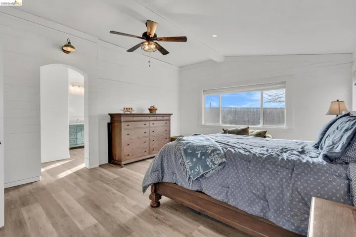 Bedroom with light wood-style floors, arched walkways, a ceiling fan, and lofted ceiling with beams