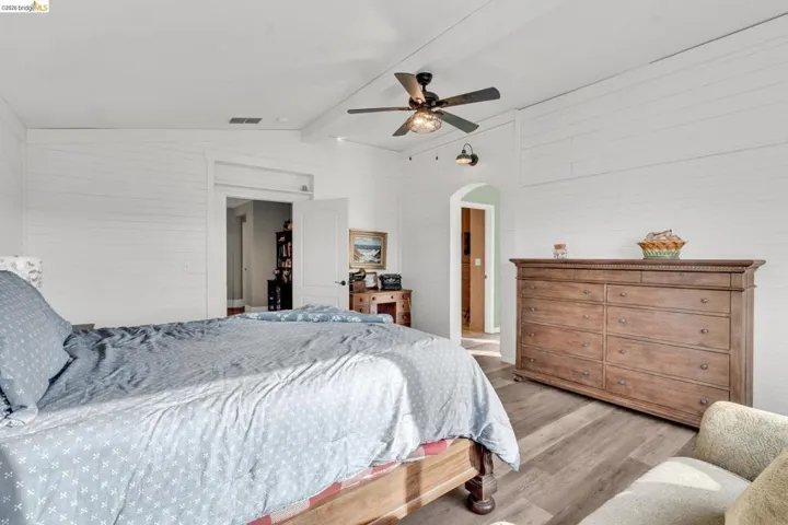 Bedroom with arched walkways, light wood-style floors, vaulted ceiling with beams, and a ceiling fan