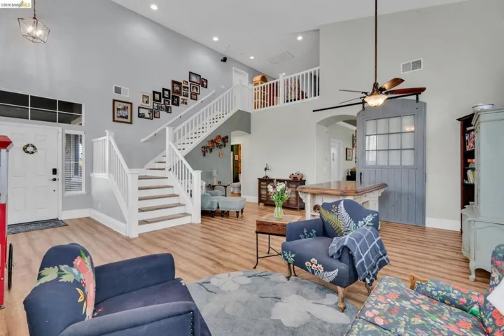 Living area with light wood finished floors, arched walkways, a high ceiling, a ceiling fan, and recessed lighting