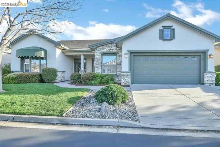 View of front of property featuring stone siding, a front lawn, stucco siding, driveway, and an attached garage
