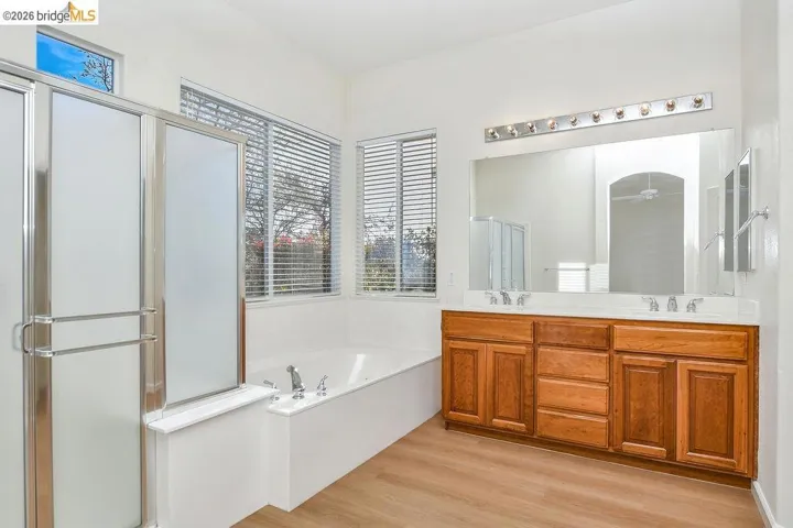Bathroom with double vanity, a garden tub, light wood-type flooring, and a shower stall