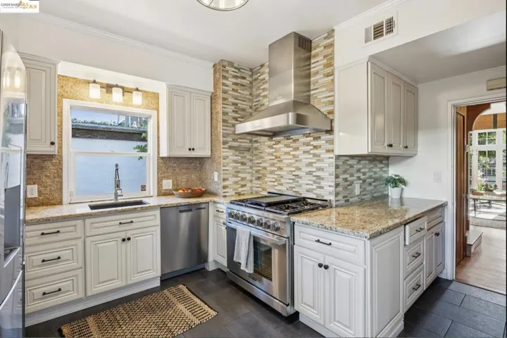 Kitchen with stainless steel appliances, light stone counters, ornamental molding, tasteful backsplash, and white cabinetry
