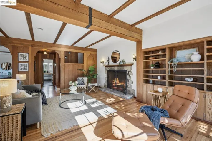 Living area with wood finished floors, beam ceiling, arched walkways, a warm lit fireplace, and wood walls