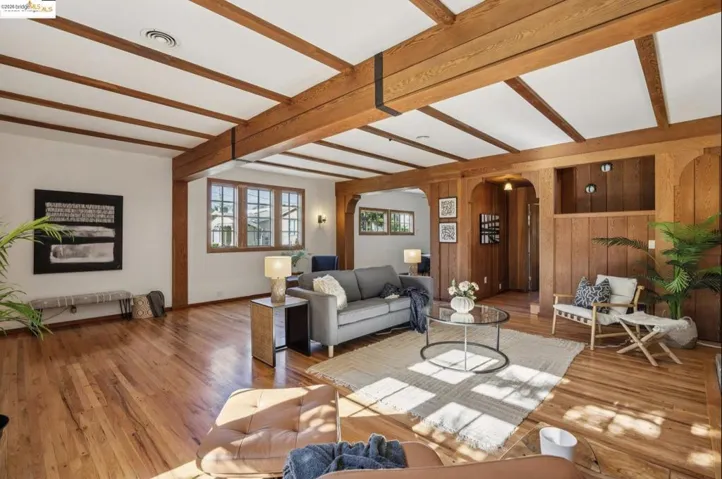 Living room with arched walkways, wood walls, beam ceiling, and wood finished floors
