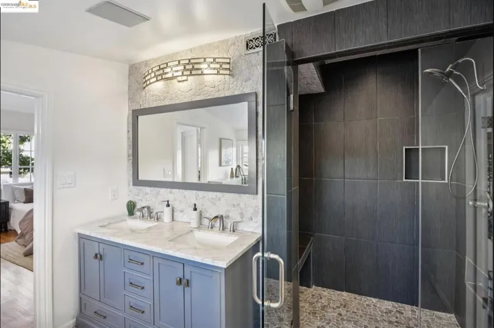 Ensuite bathroom featuring double vanity, a shower stall, and decorative backsplash