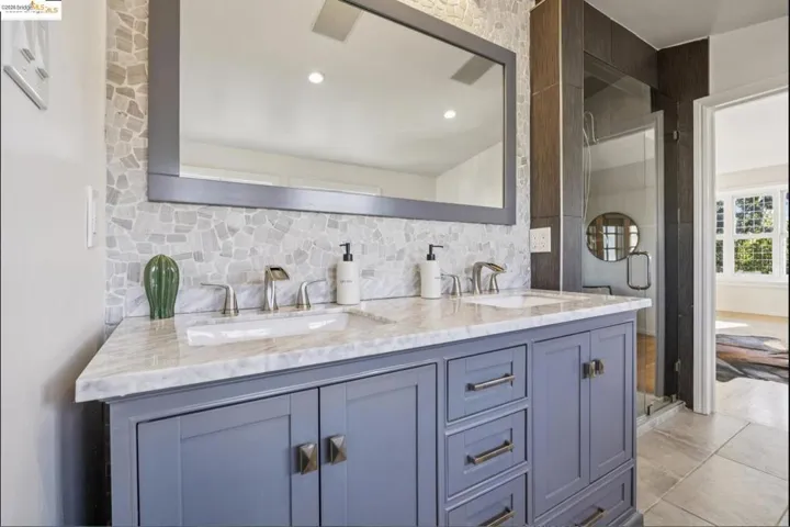 Full bathroom featuring double vanity, a shower stall, tasteful backsplash, and light tile patterned floors