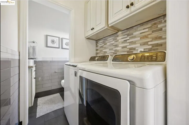 Laundry room with independent washer and dryer, tile walls, cabinet space, and dark tile patterned floors