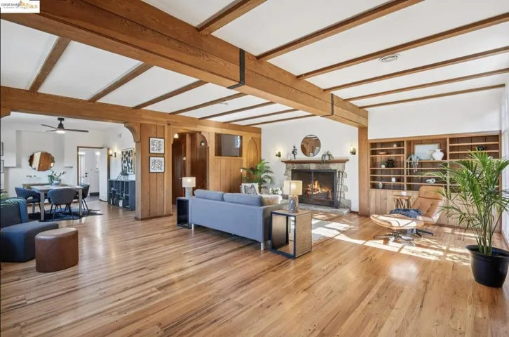 Living room featuring light wood-type flooring, beam ceiling, a fireplace, arched walkways, and wood walls