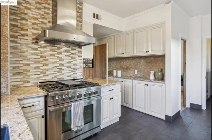 Kitchen with stainless steel range with gas stovetop, light stone countertops, decorative backsplash, ornamental molding, and dark tile patterned floors